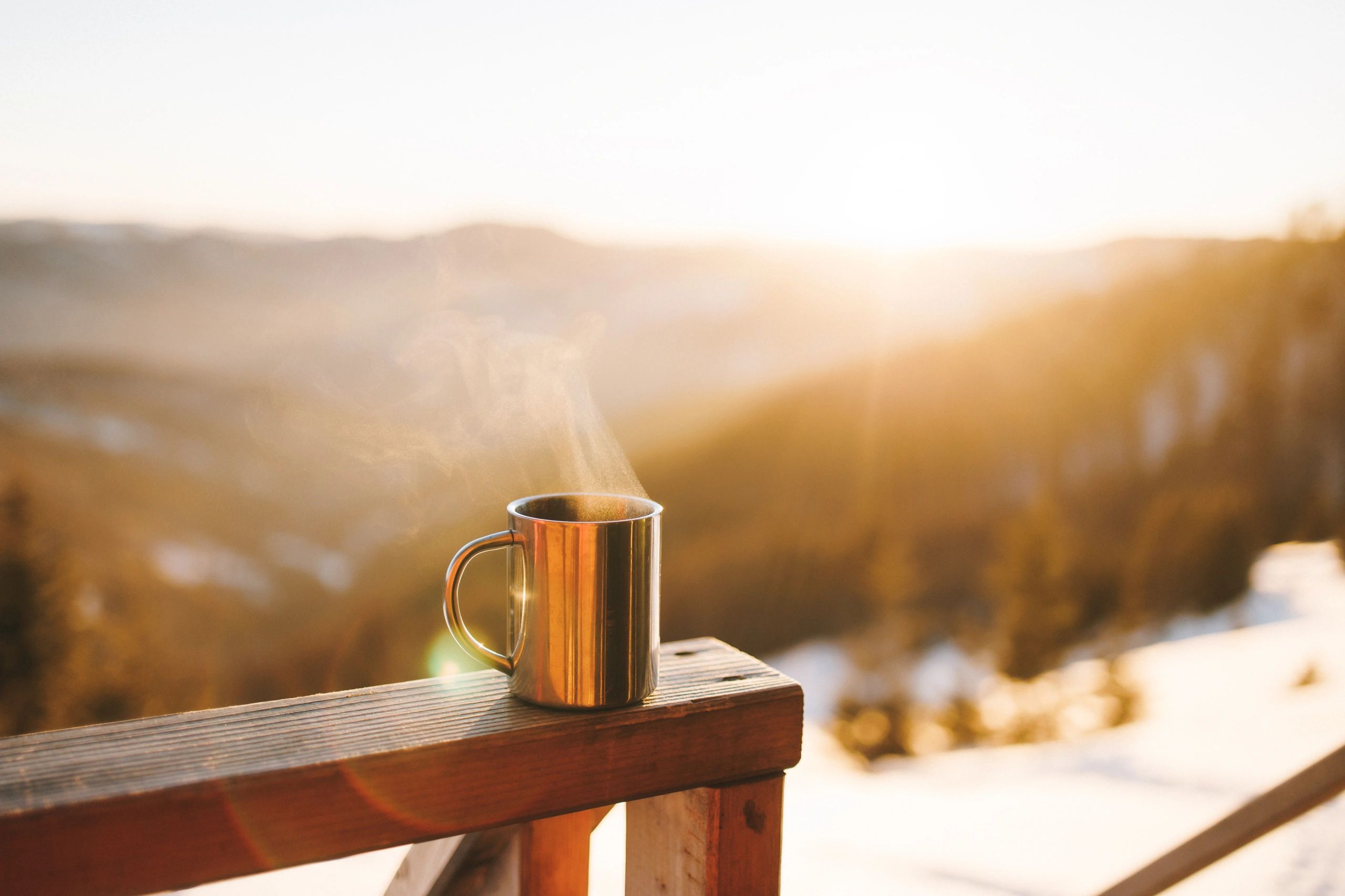Warm mug held outdoors at sunrise, suggesting calm reflection.